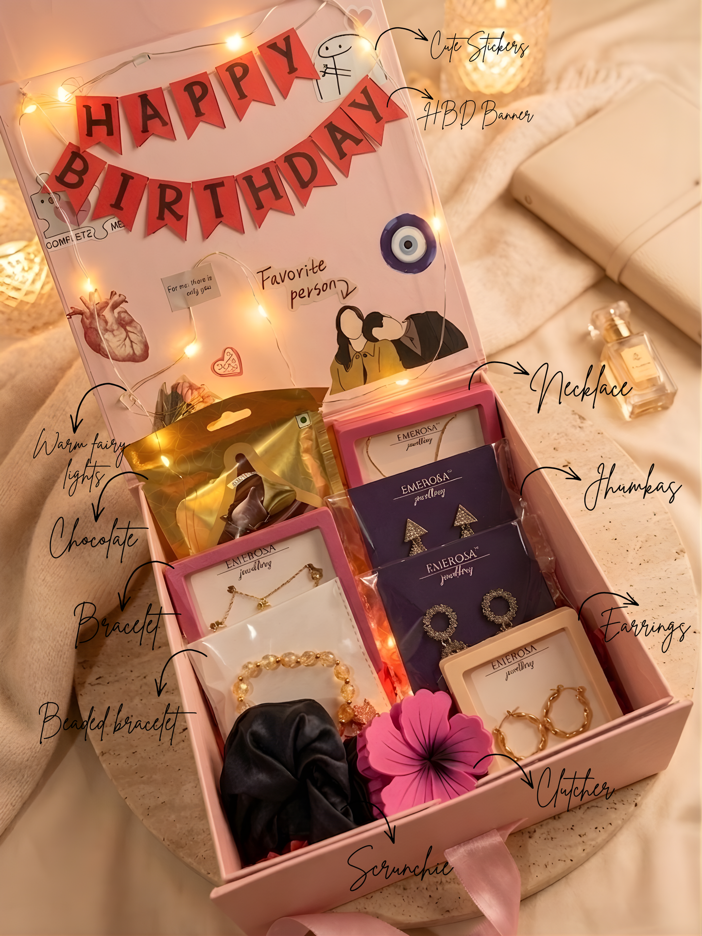 Gift box with birthday-themed items and decorative lights on a soft surface.