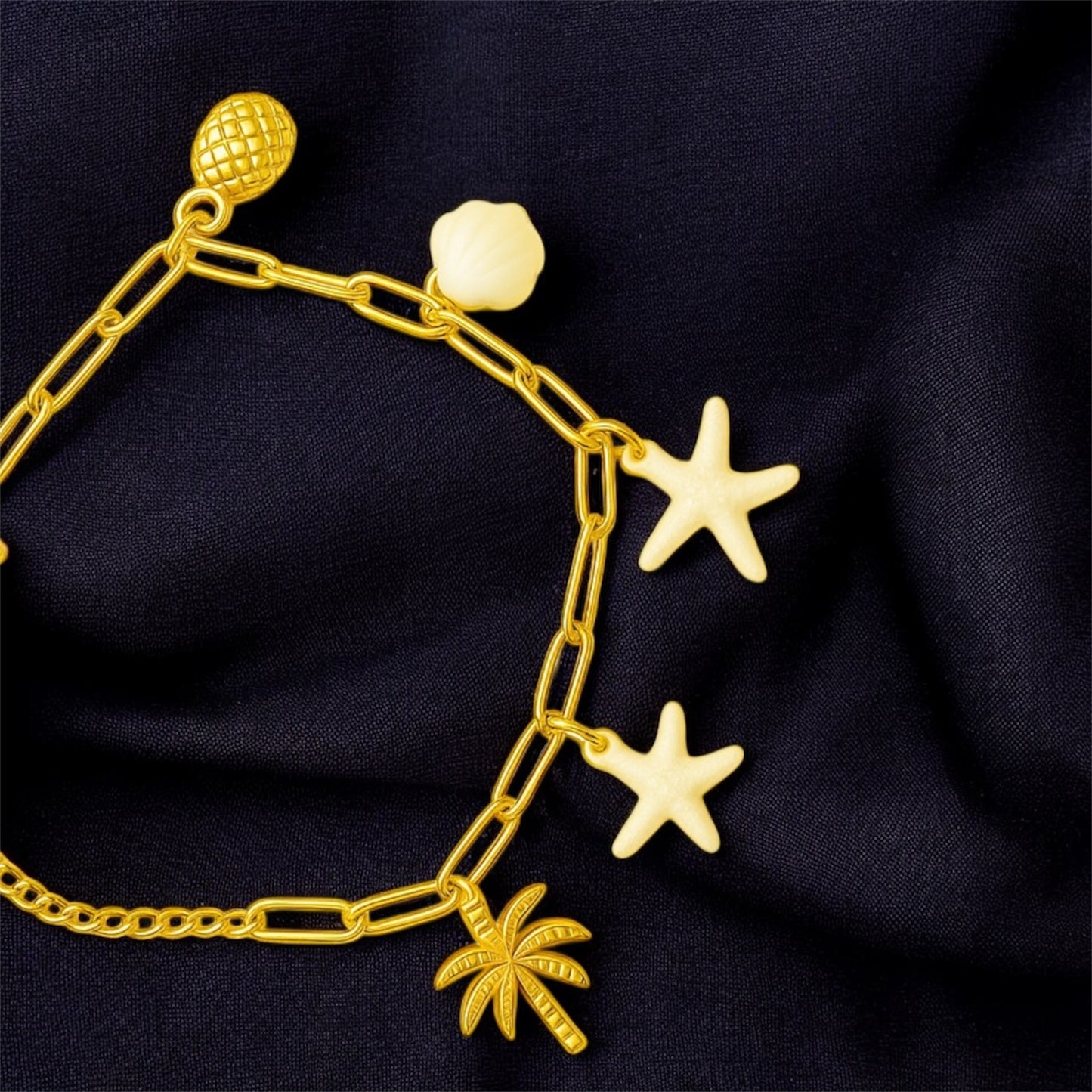 Gold bracelet with star and palm tree charms on a dark fabric background