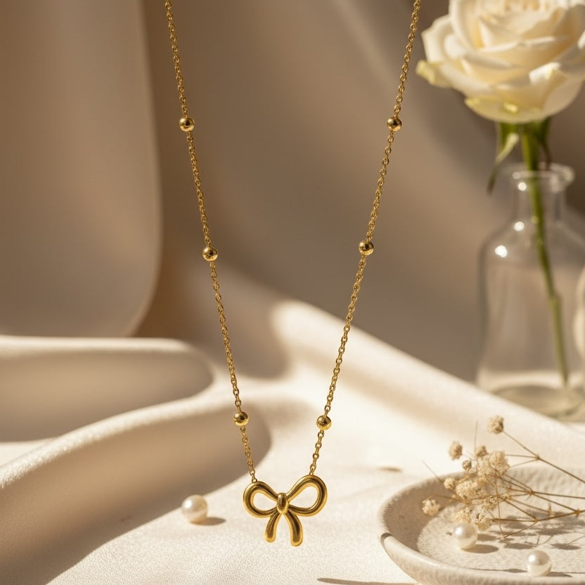 Gold necklace with a bow pendant on a white surface with a white rose in the background